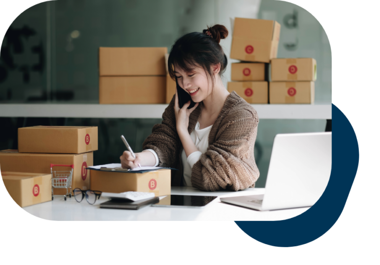 woman in warehouse calling someone while writing on a clipboard